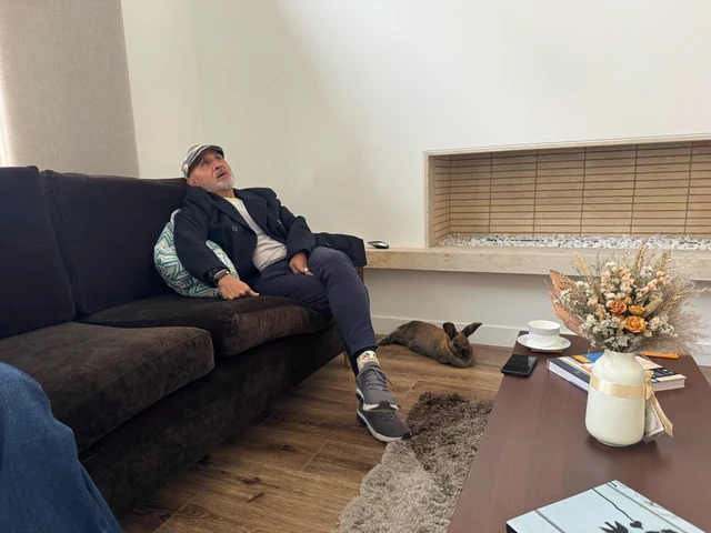 Coco descansando en el suelo de la sala, junto a una persona sentada en el sofá.